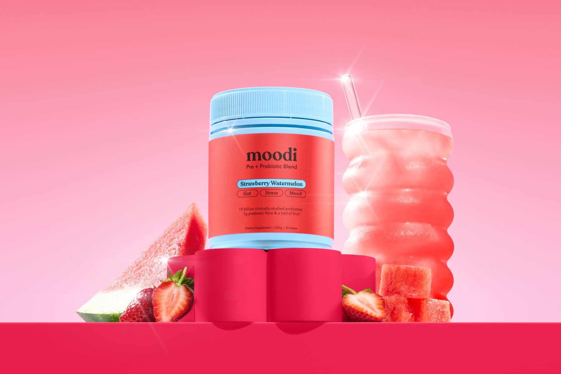 Container of Moodi probiotic mix with watermelon and strawberry on pink background.
