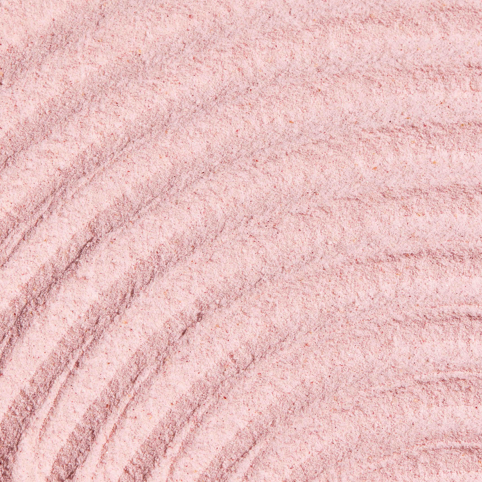 Smooth, raked patterns in pink sand.