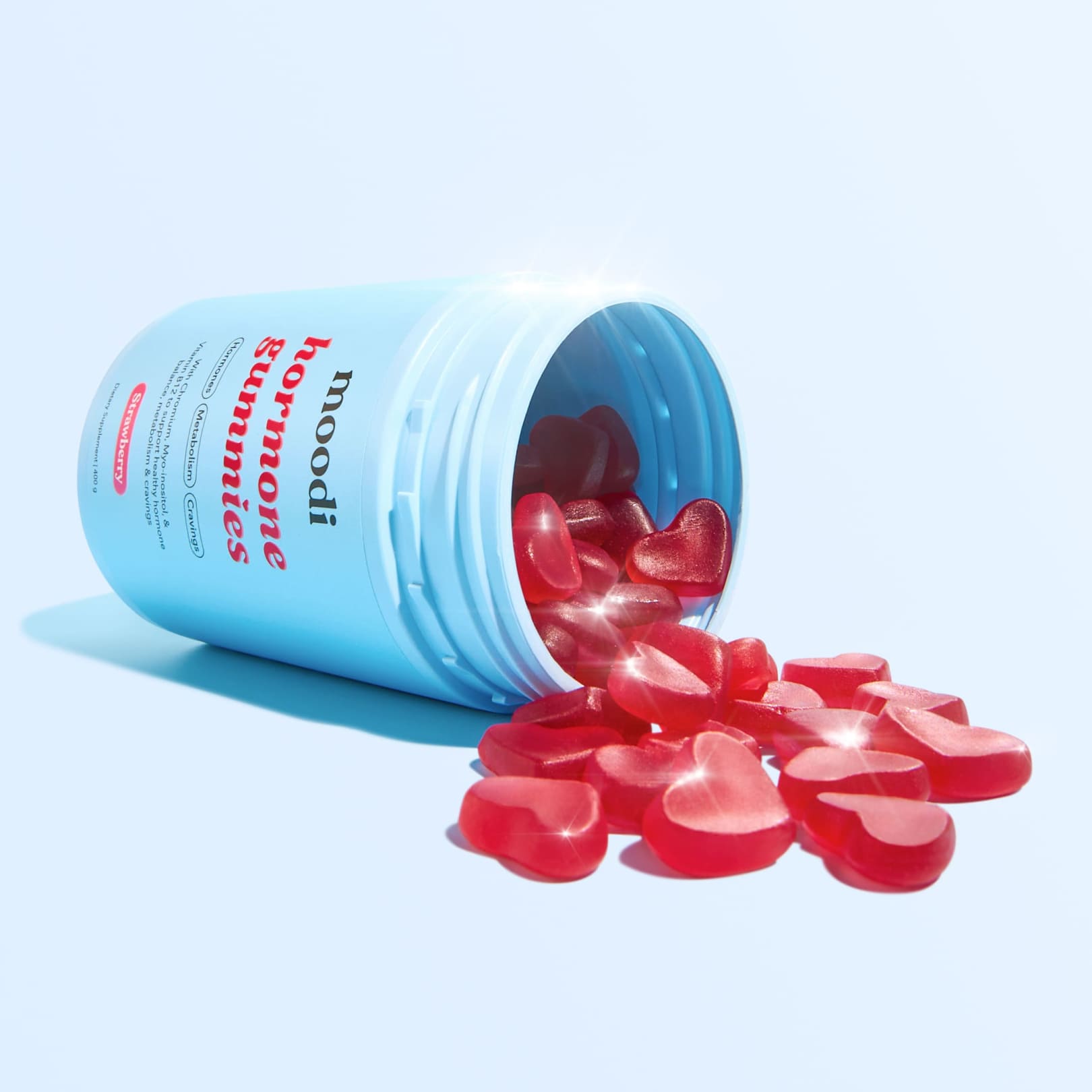 A blue bottle of 'moodi hormone gummies' on its side, with red, heart-shaped gummies spilling out.