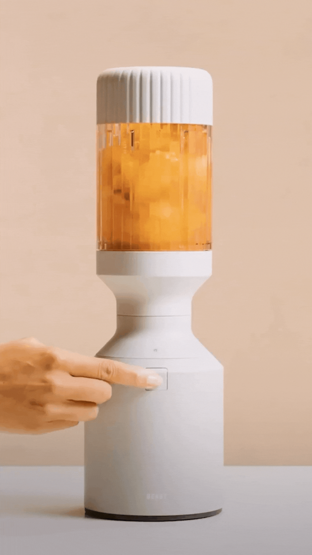 Hand pressing button on a white blender with orange contents.