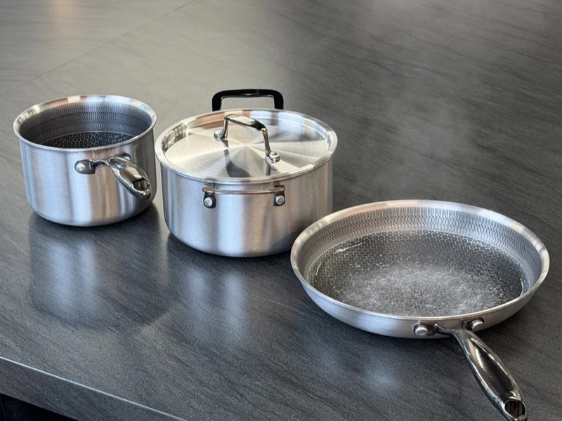A stainless steel cookware set with a honeycomb pattern, including a frying pan with boiling water.