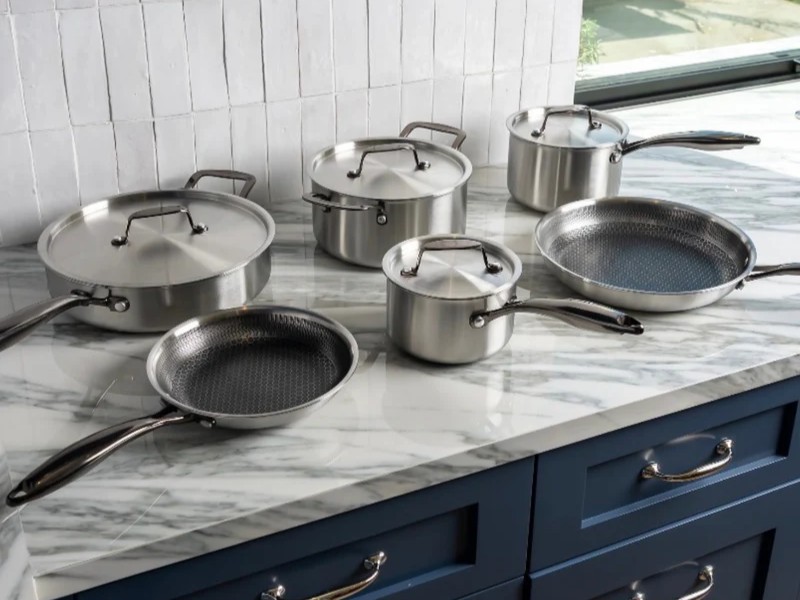 A stainless steel cookware set with pots and pans displayed on a marble kitchen countertop.