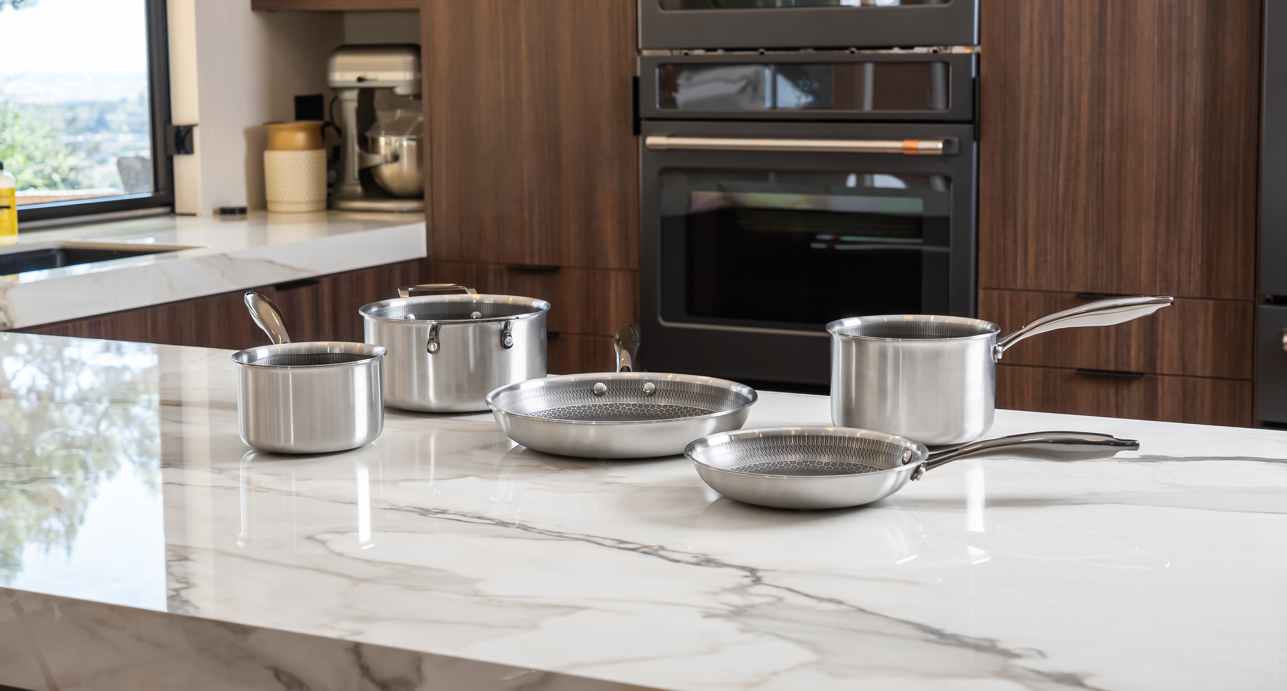 A set of stainless steel pots and pans sit on a white marble kitchen island.