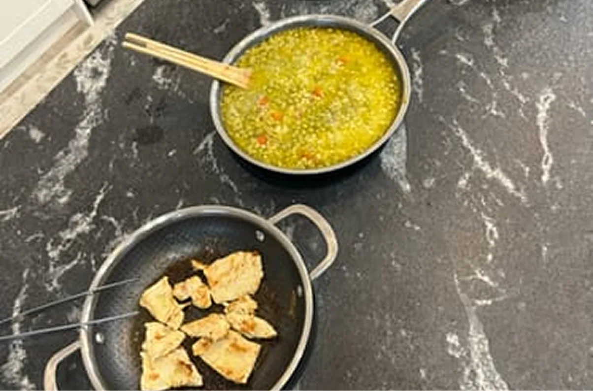 Two pans of food, one with a yellow soup and one with seared chicken, on a countertop.