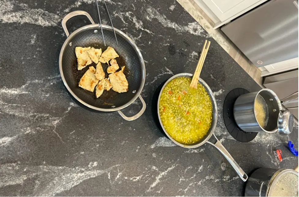 An overhead view of several pots and pans with food cooking on a dark marbled countertop.