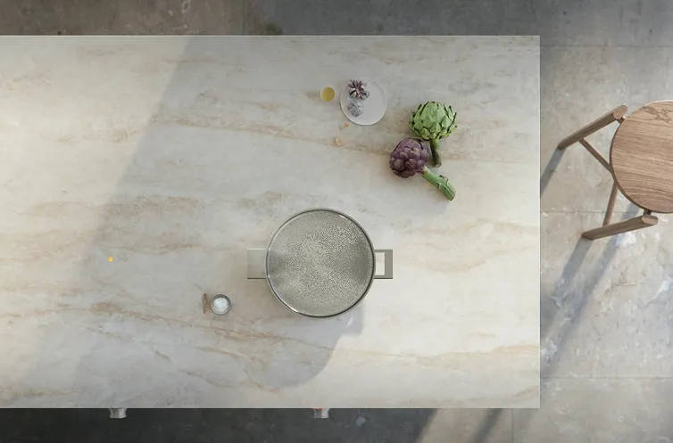 Overhead view of a pot, artichokes, and a plate on a marble countertop next to a stool.