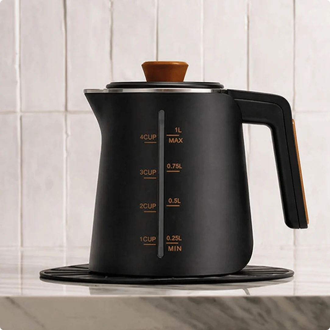 A matte black electric kettle with wooden accents sits on a kitchen countertop in front of a tiled wall.