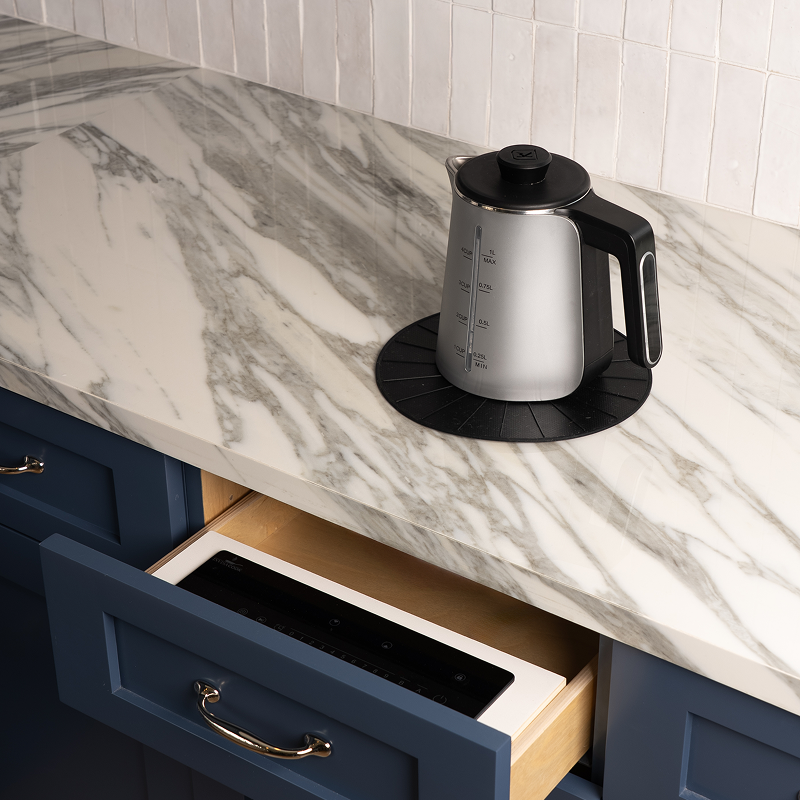 An electric kettle on a marble countertop with a cooktop visible in an open drawer below.