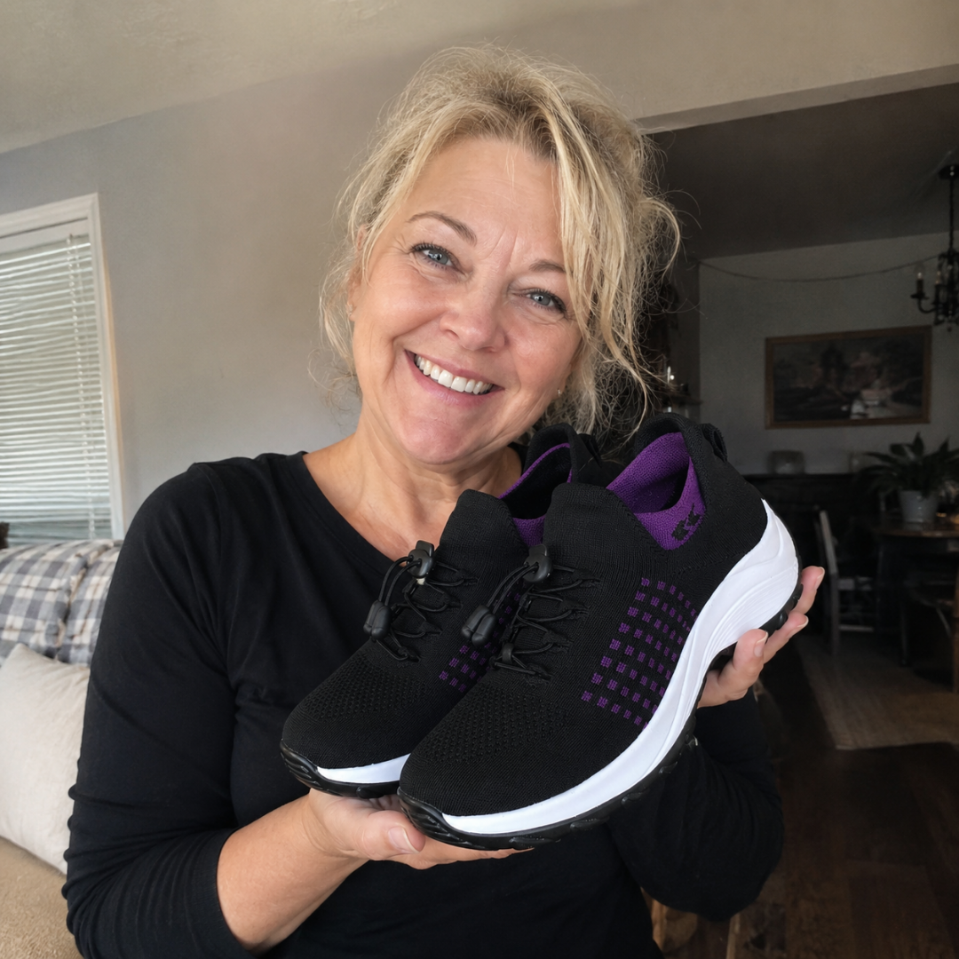 A smiling blonde woman holds up a pair of black and purple sneakers with white soles.