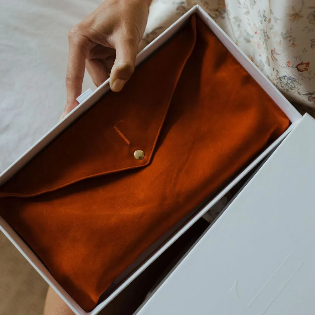 Person holding an orange, envelope-style pouch in a white box.
