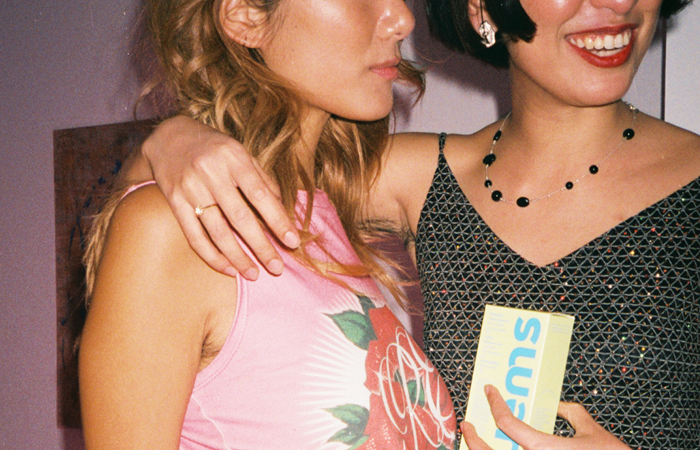 Two people smiling, one holding a box labeled 'gems', in a casual setting.