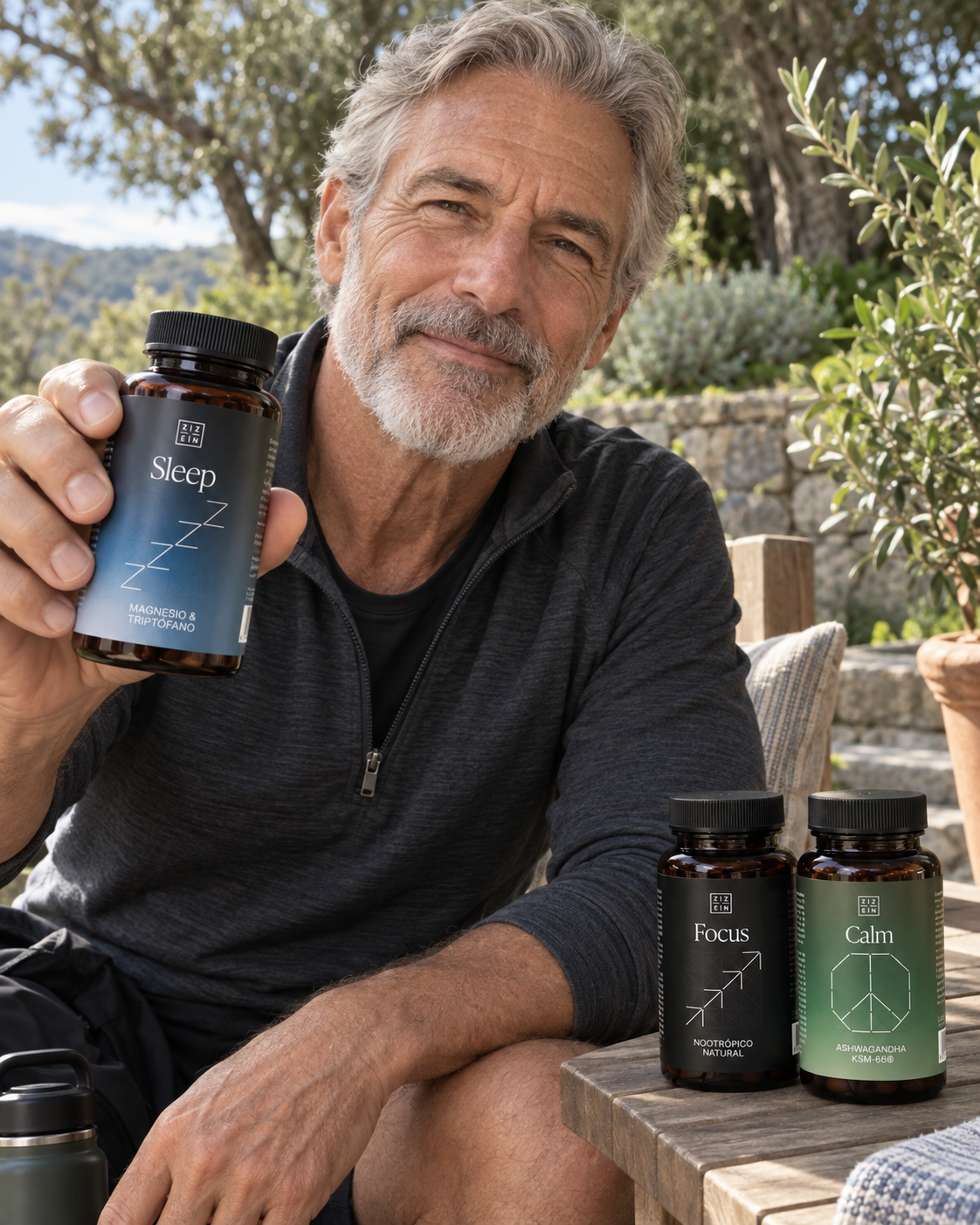A gray-haired man sits outside, holding a bottle of 'Sleep' supplements, with other bottles on a table.