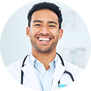A smiling man wearing a white lab coat with a stethoscope around his neck.