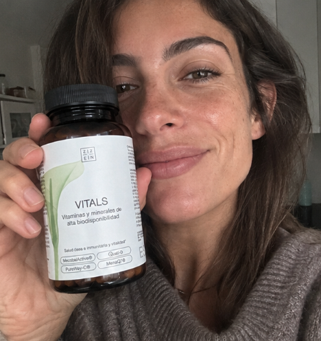 A smiling woman holds a bottle of Ziz Ein Vitals vitamins and minerals up to the camera.