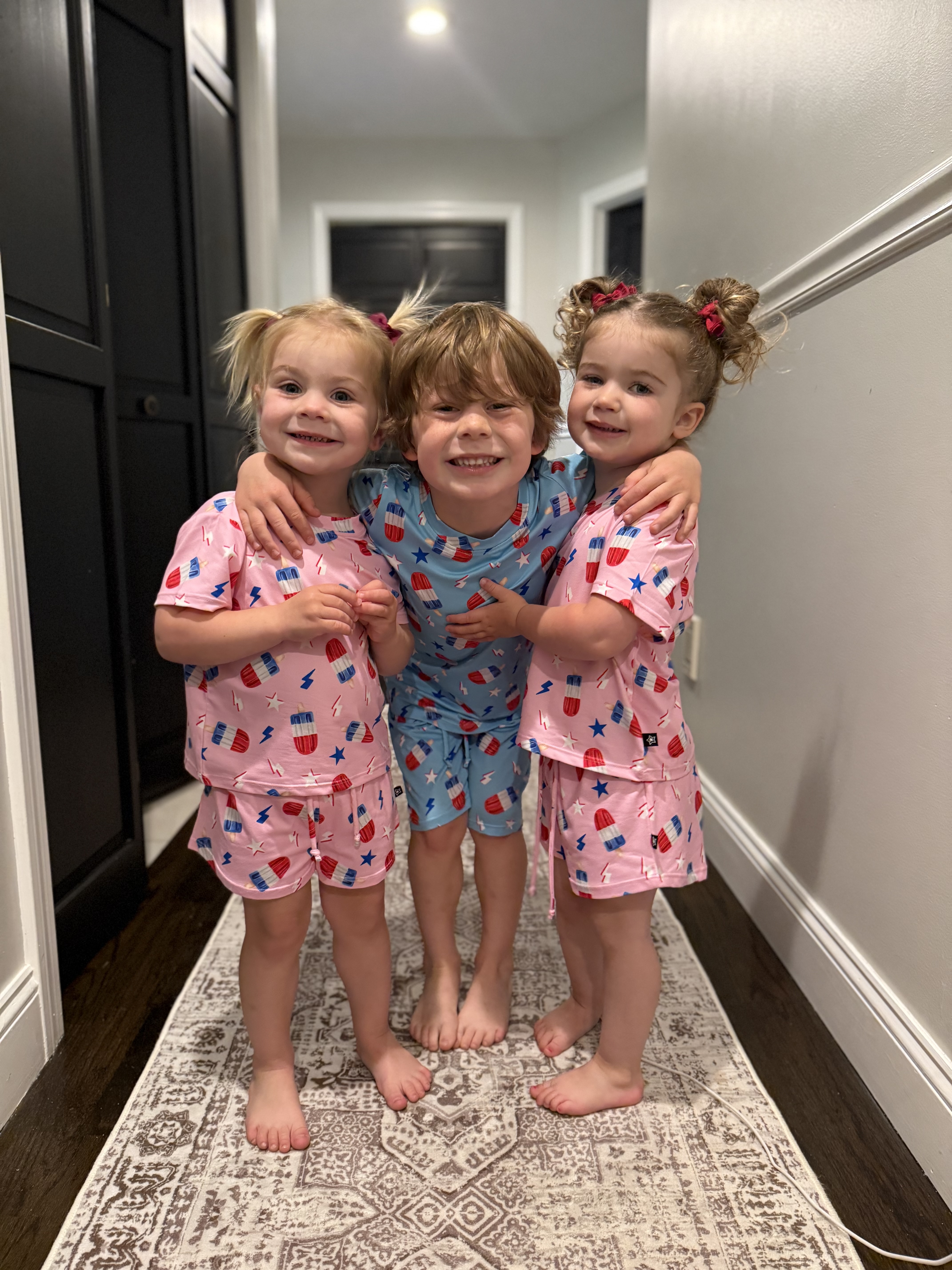 Three children in matching pajamas smiling in a hallway.
