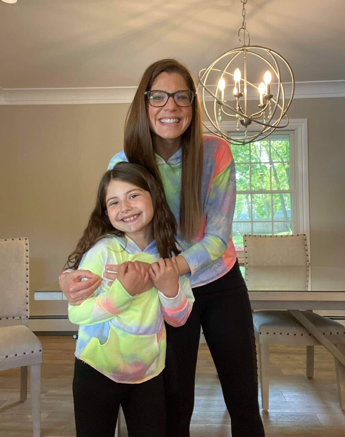 Two people smiling, wearing matching tie-dye hoodies in a dining room.