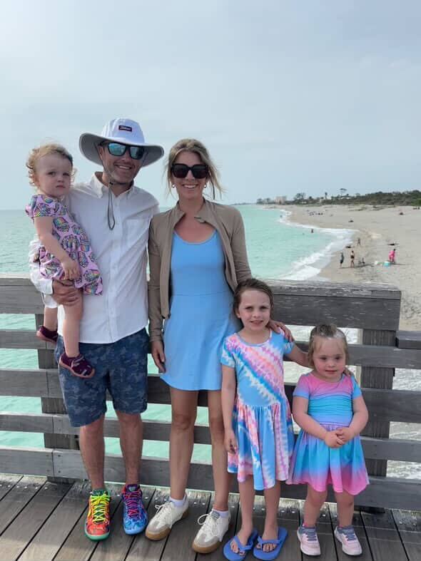 A family of five posing on a boardwalk by the beach.