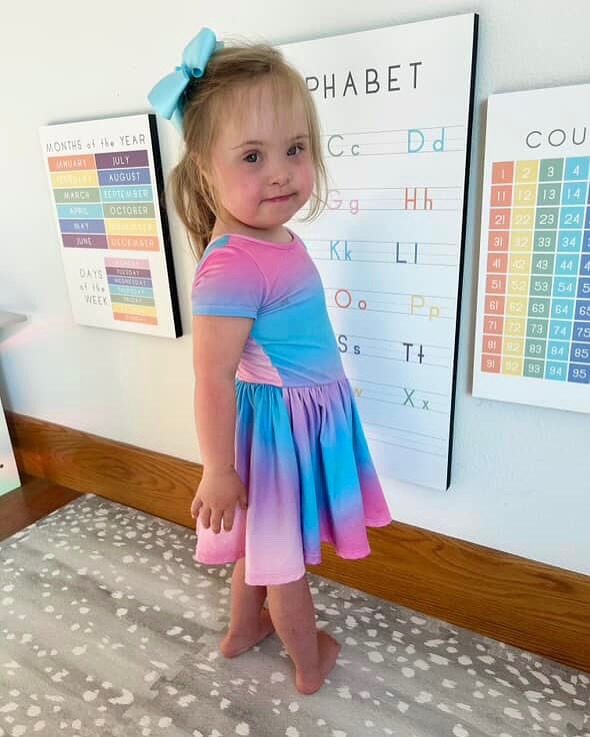 Young girl in a colorful dress standing by educational posters.