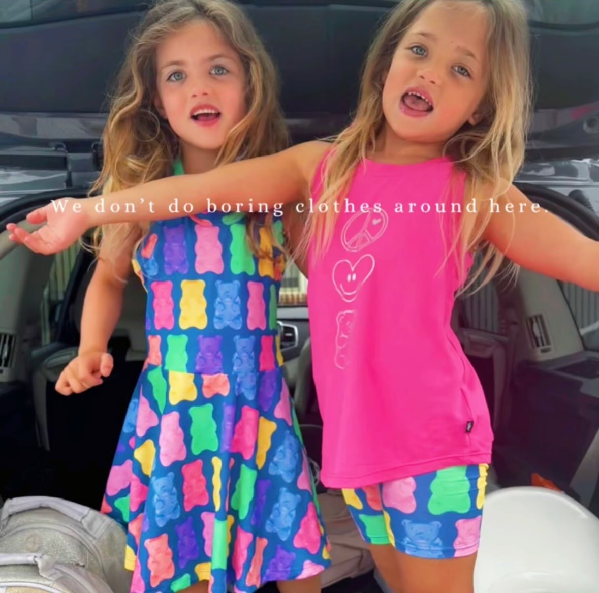 Two children in colorful clothing standing in a car trunk.