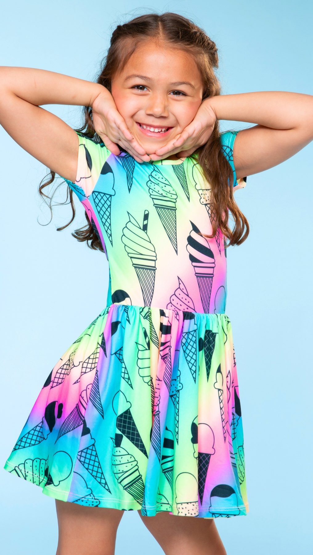 Smiling child in a colorful ice cream-patterned dress against a blue background.