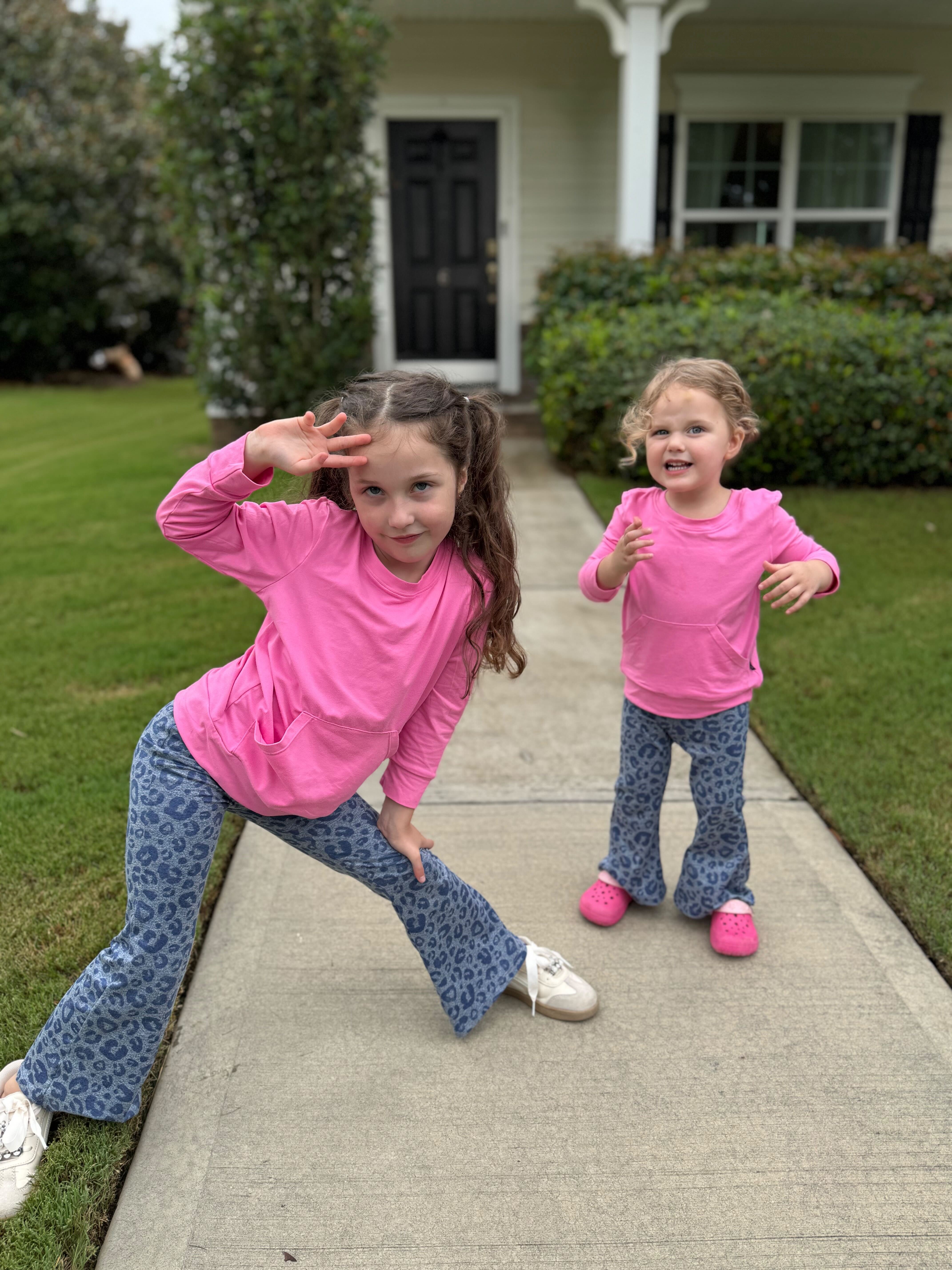 Two children in pink tops and blue patterned pants posing on a sidewalk.
