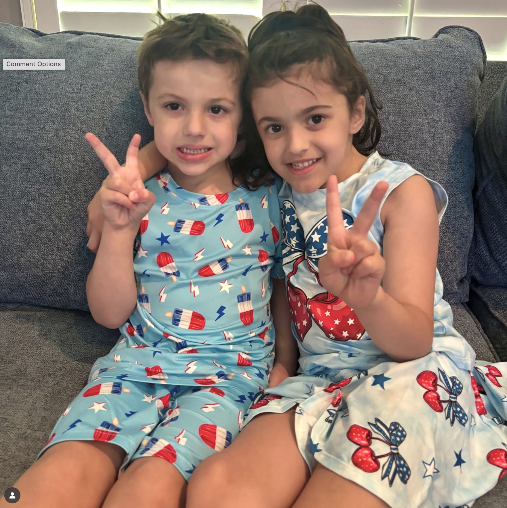 Two children sitting on a sofa, each showing a peace sign.