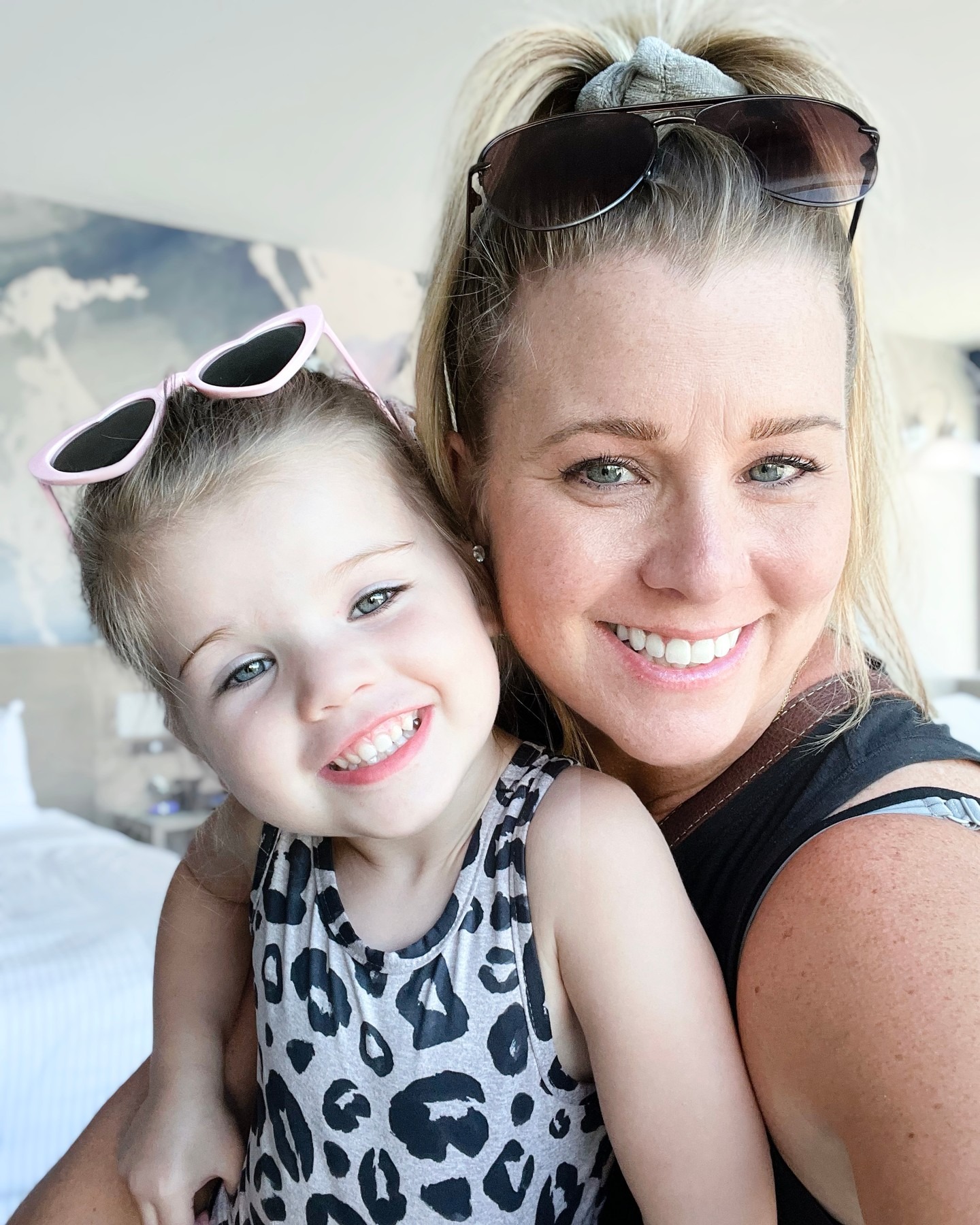 A woman and child smiling together indoors, both wearing sunglasses.
