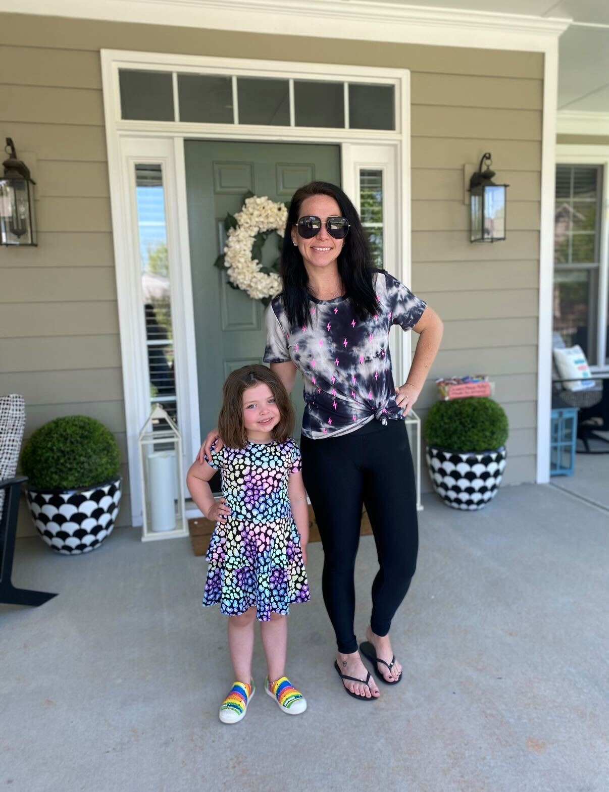 Woman and child smiling on a porch with decorative plants.