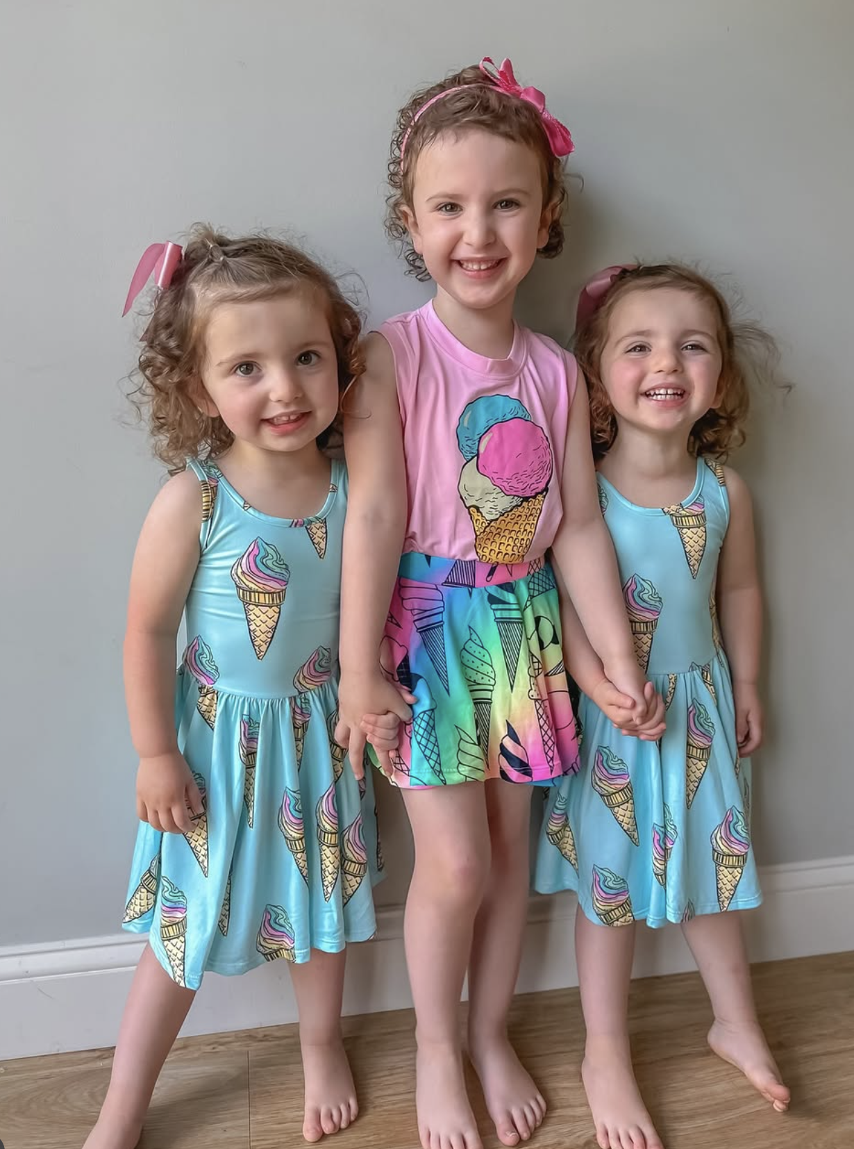 Three children smiling, wearing dresses with ice cream cone designs.