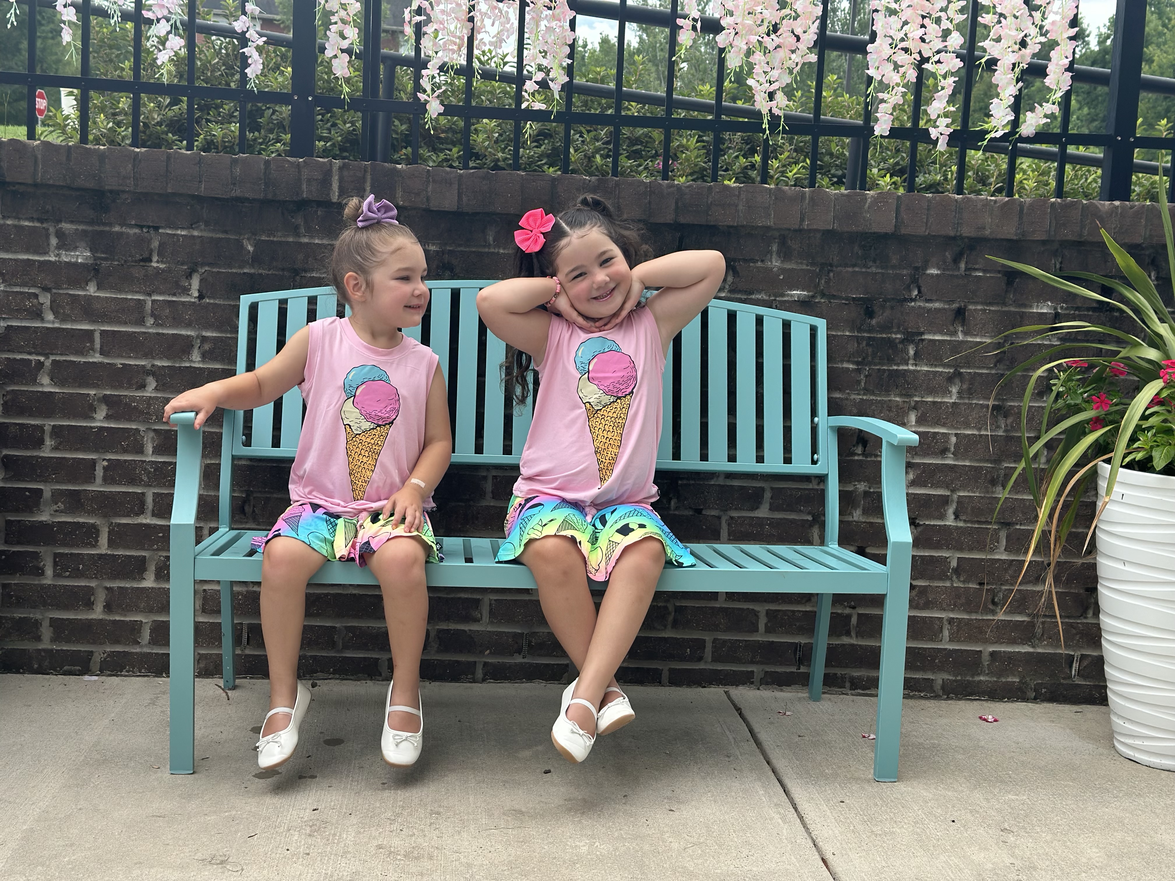 Two children in matching outfits sit on a turquoise bench, smiling.