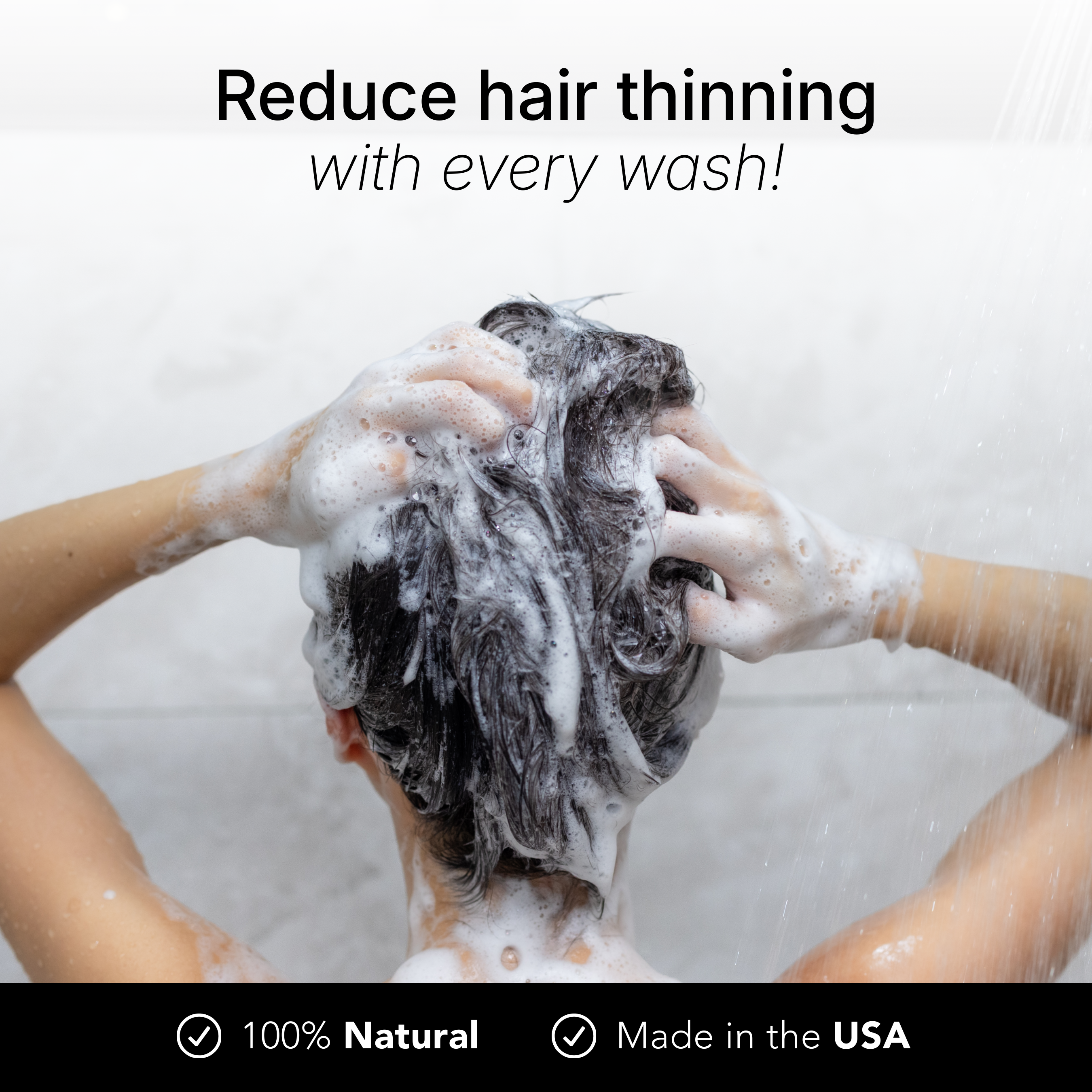 A person, seen from behind, washes their dark hair with a thick lather of shampoo in the shower.