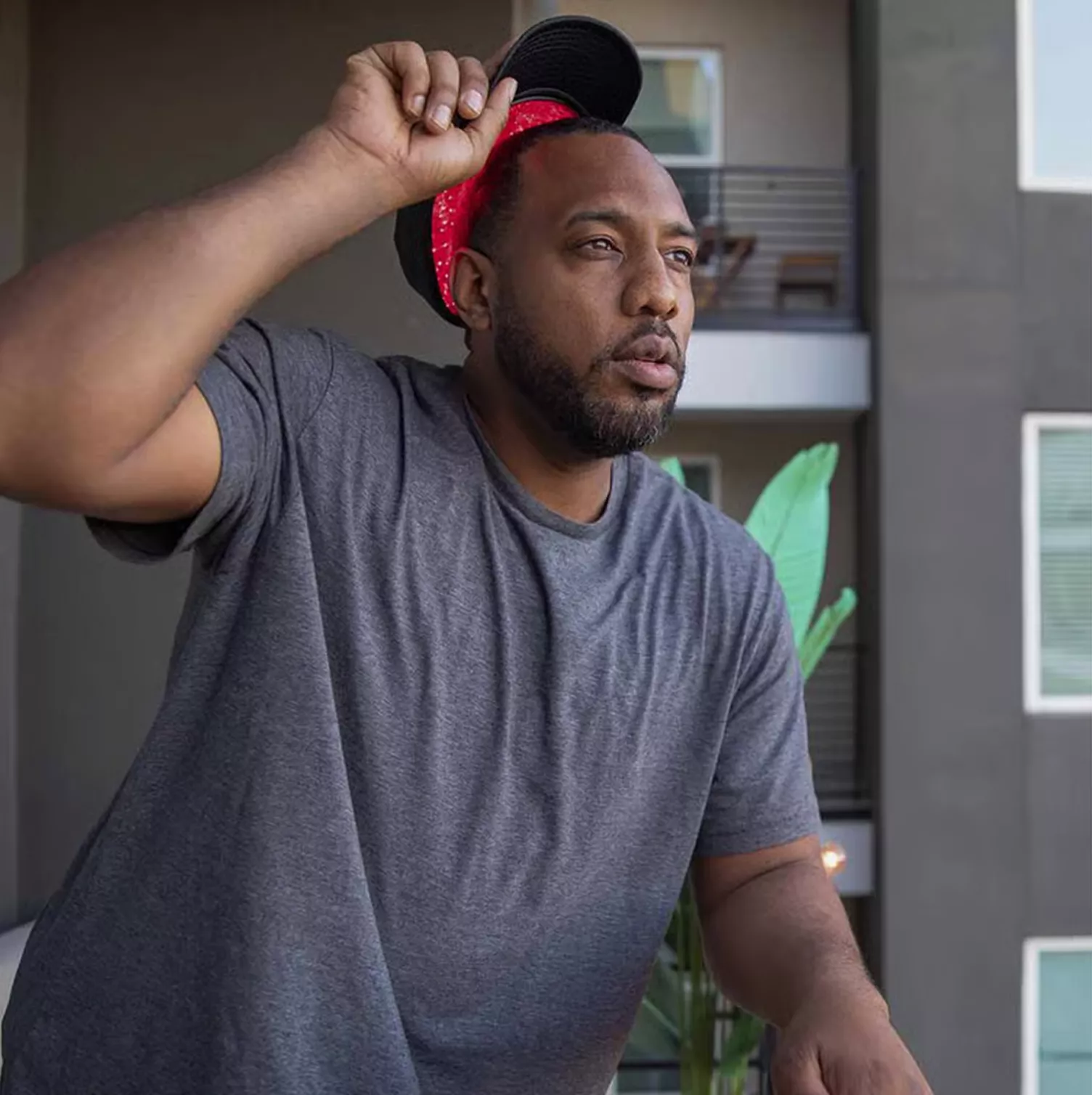 A man in a grey t-shirt and a backward cap over a red bandana looks off to the side.
