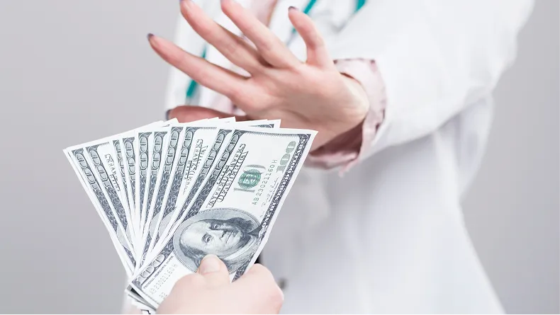A person in a white coat holds up their hand, refusing a fan of one-hundred-dollar bills.