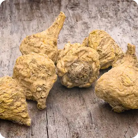 A close-up of several dried maca roots with their stems attached, resting on a weathered wooden surface.