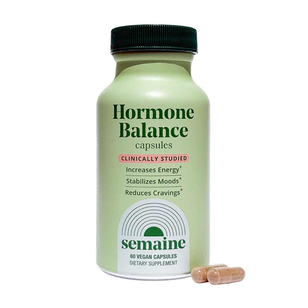 A bottle of Semaine Hormone Balance capsules with two capsules sitting next to it on a black background.
