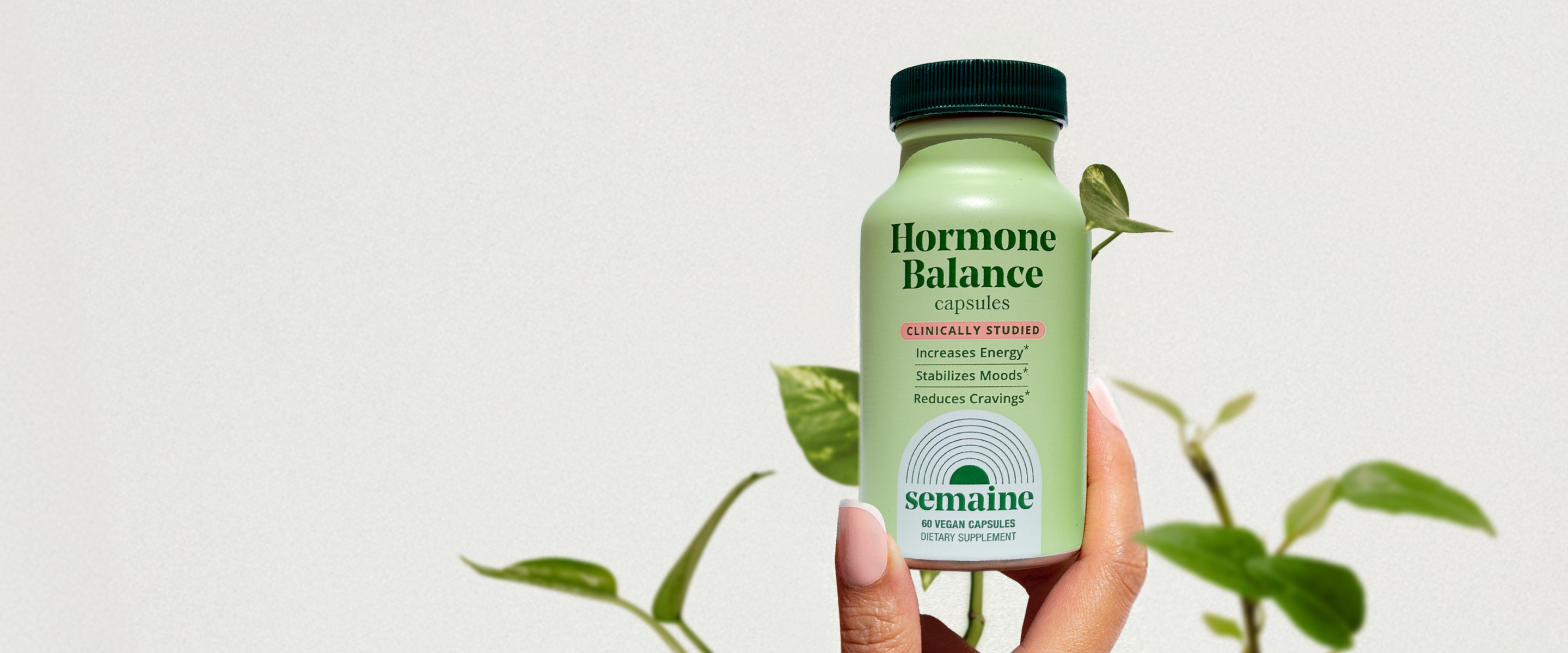 A hand holds a bottle of Semaine Hormone Balance capsules in front of a leafy plant.