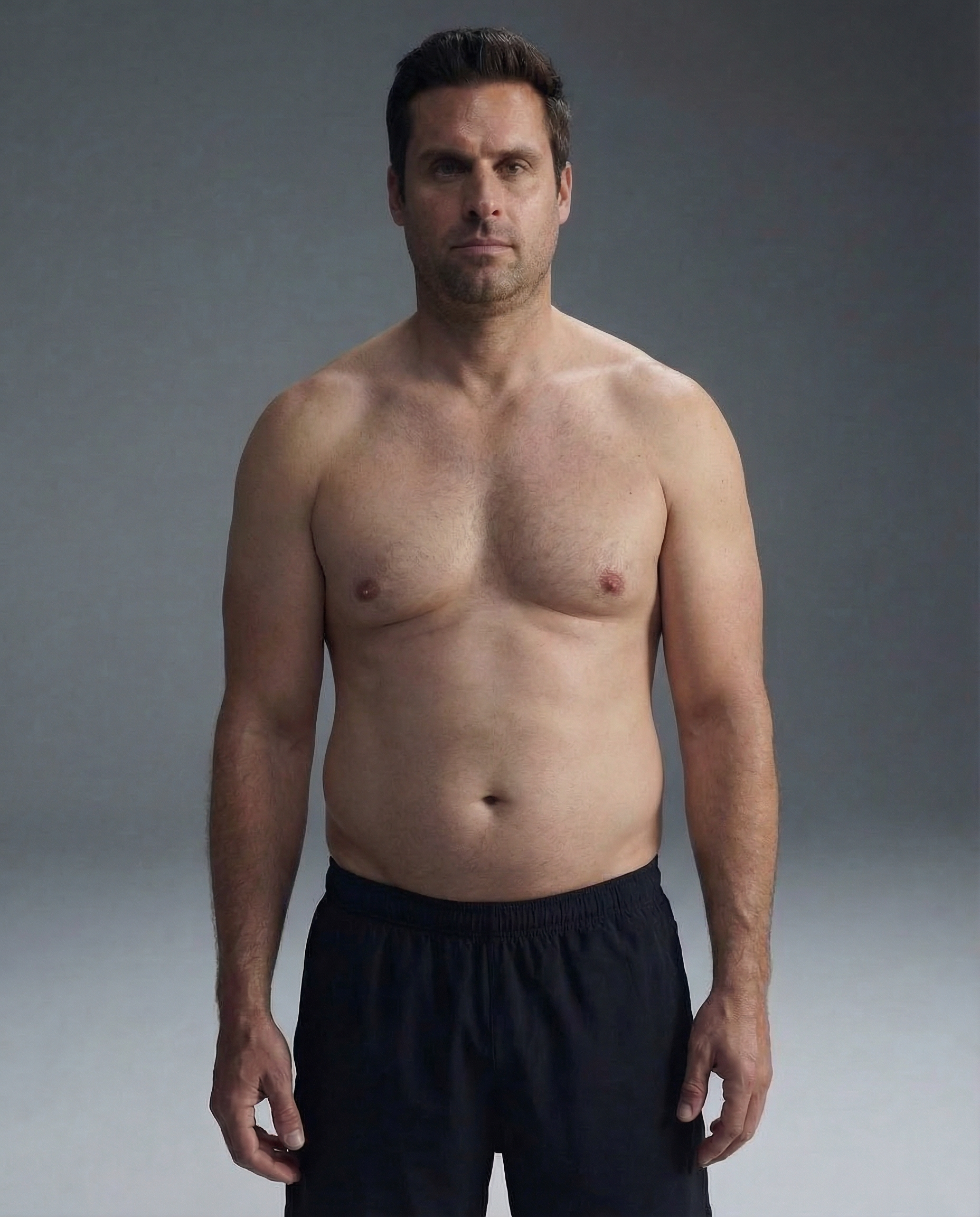 A shirtless man in black shorts stands facing forward against a plain gray background.