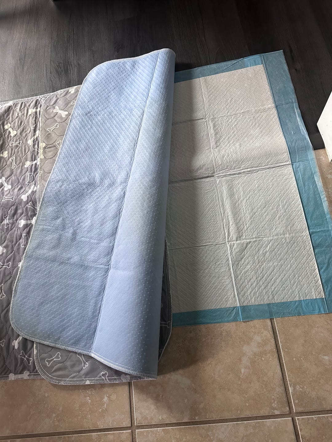 A reusable, quilted pet pad with a bone pattern is partially folded over a disposable puppy pad.