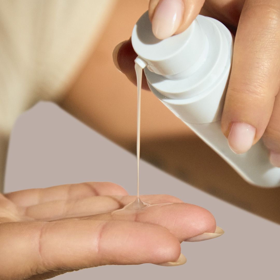 A close-up of a person dispensing a clear liquid from a white pump bottle into their hand.