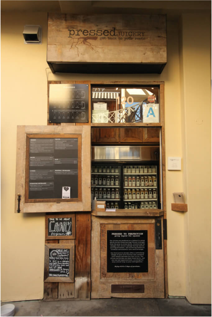 The rustic wooden storefront of a Pressed Juicery, with a window display of bottled juices.