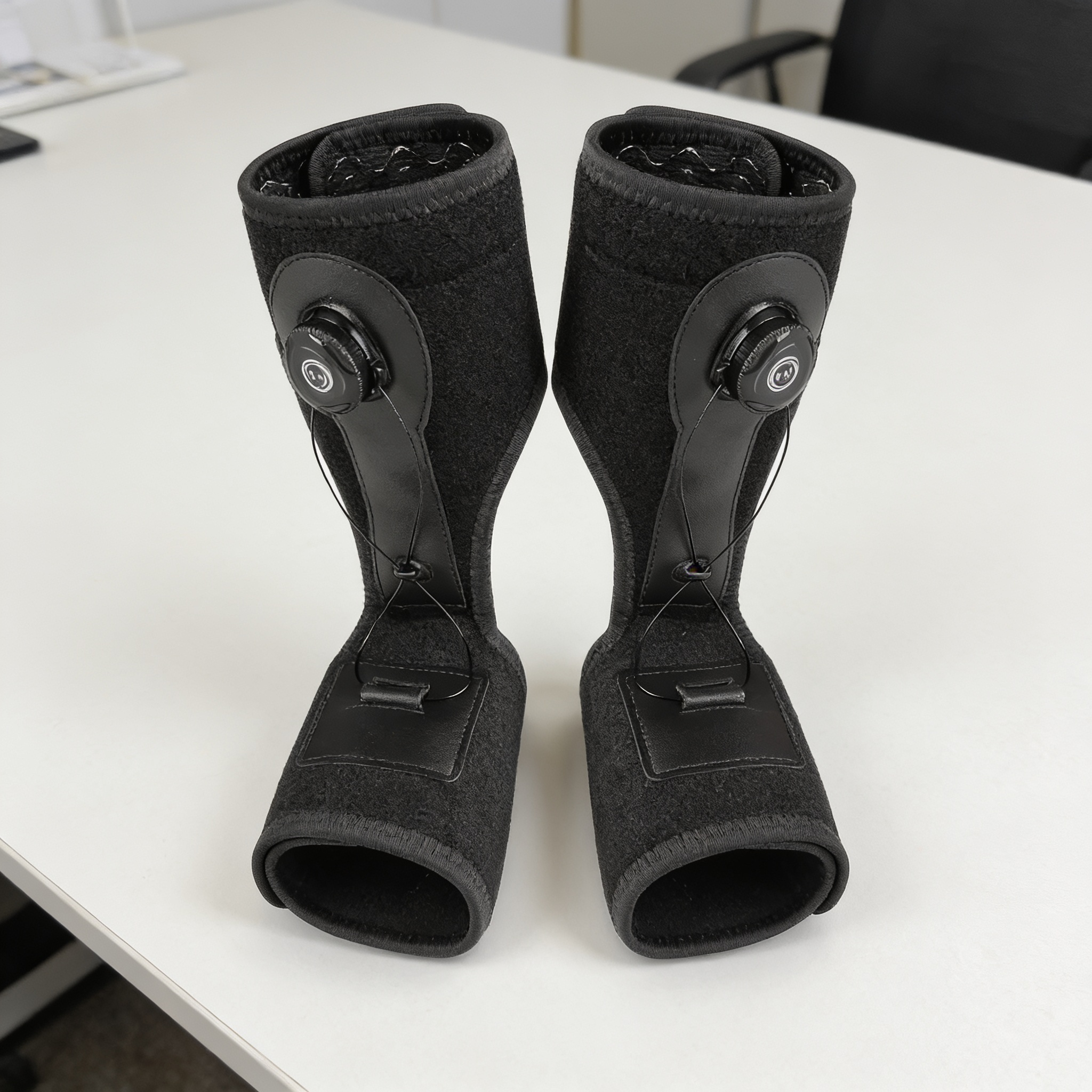 A pair of black fabric braces with adjustable dials standing upright on a white desk.