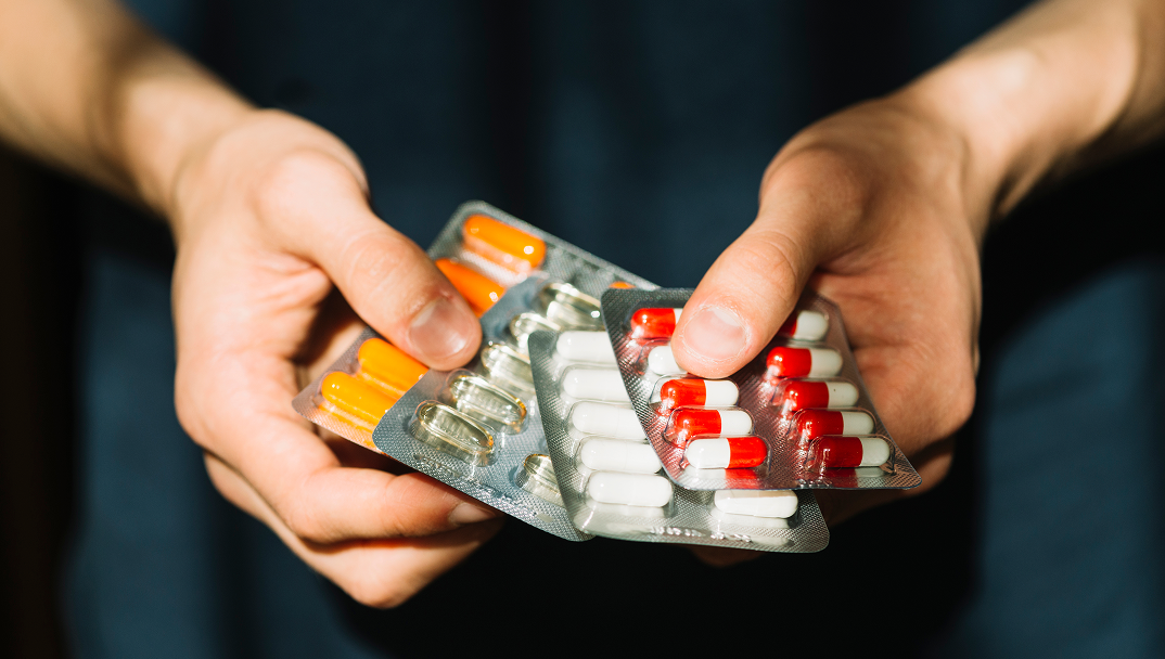Hands holding blister packs of capsules in different colors.