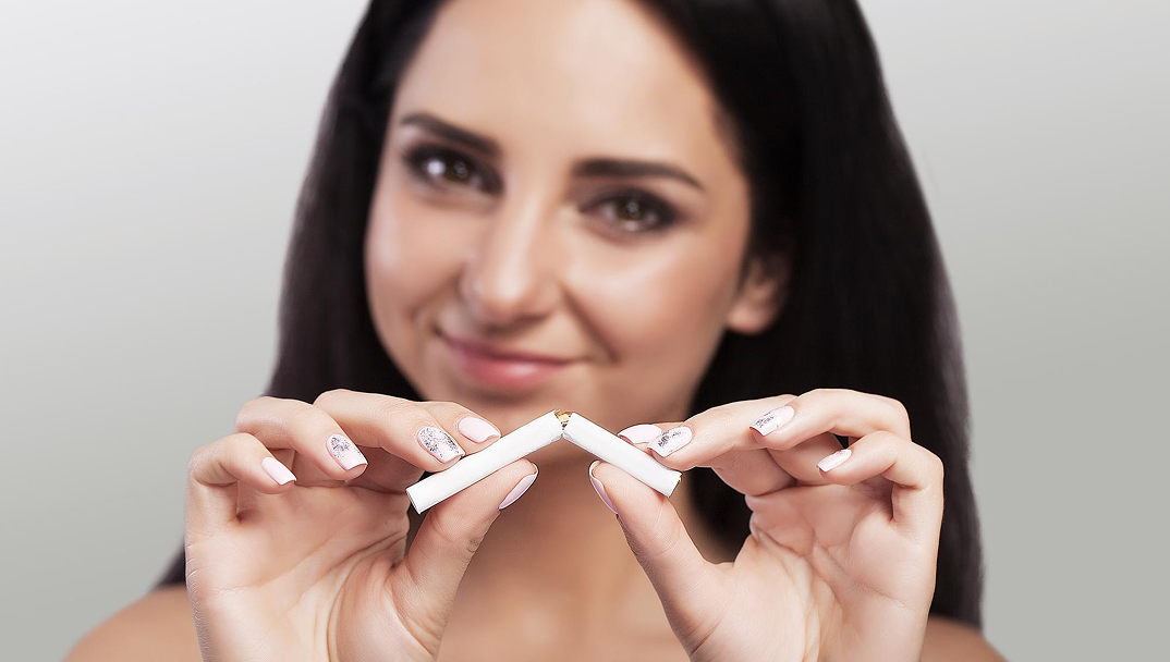 Person breaking a cigarette in half against a neutral background.
