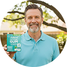 A smiling man in a blue polo shirt holds a box of Quitline Nicotine Gum outdoors.