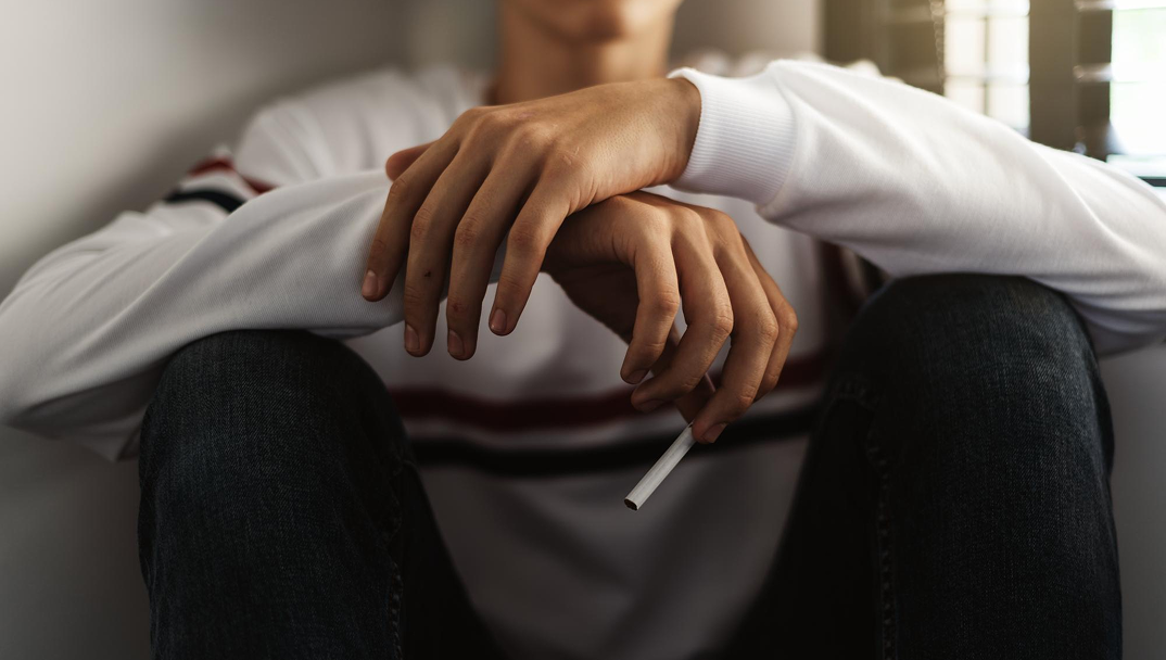 Person sitting with hands visible, holding a cigarette.