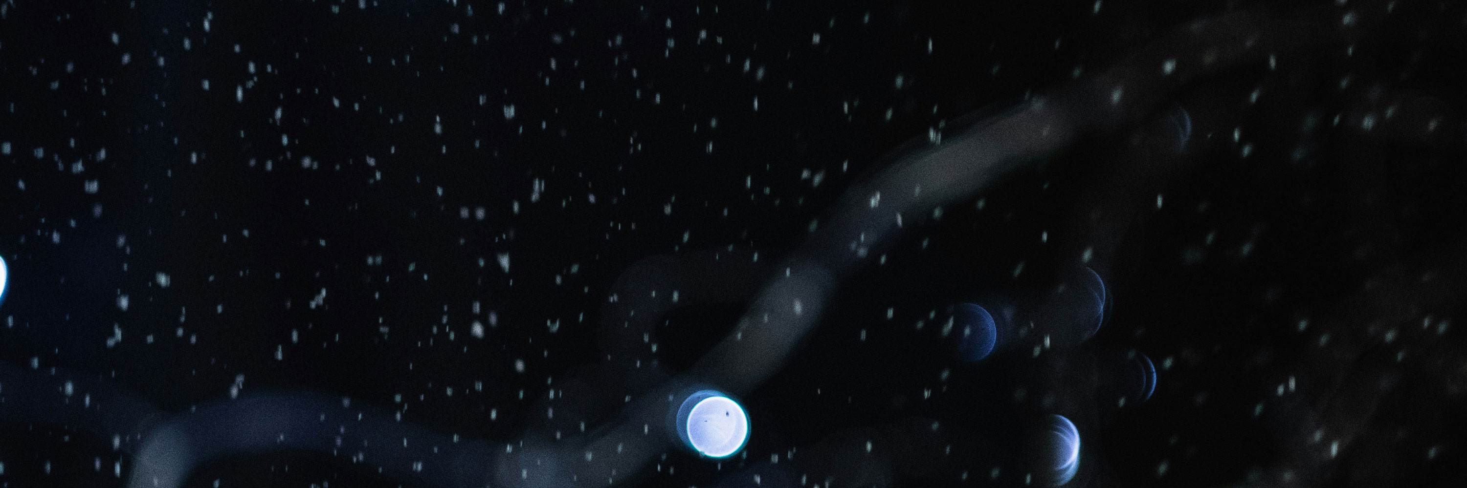 Dark abstract image with glowing orbs and scattered white specks.