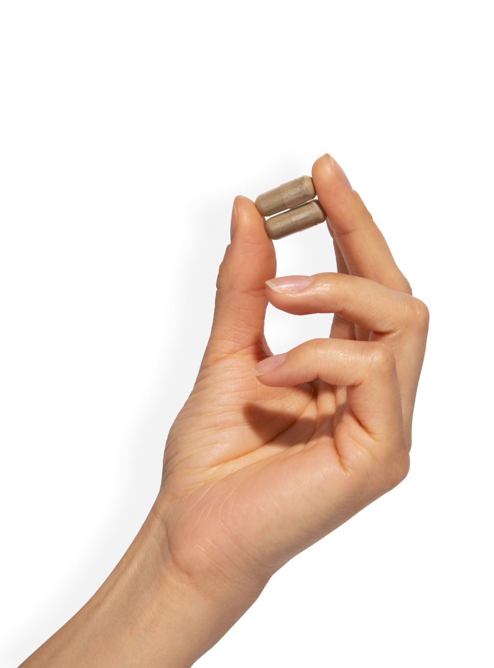 Hand holding two brown capsules against a black background.