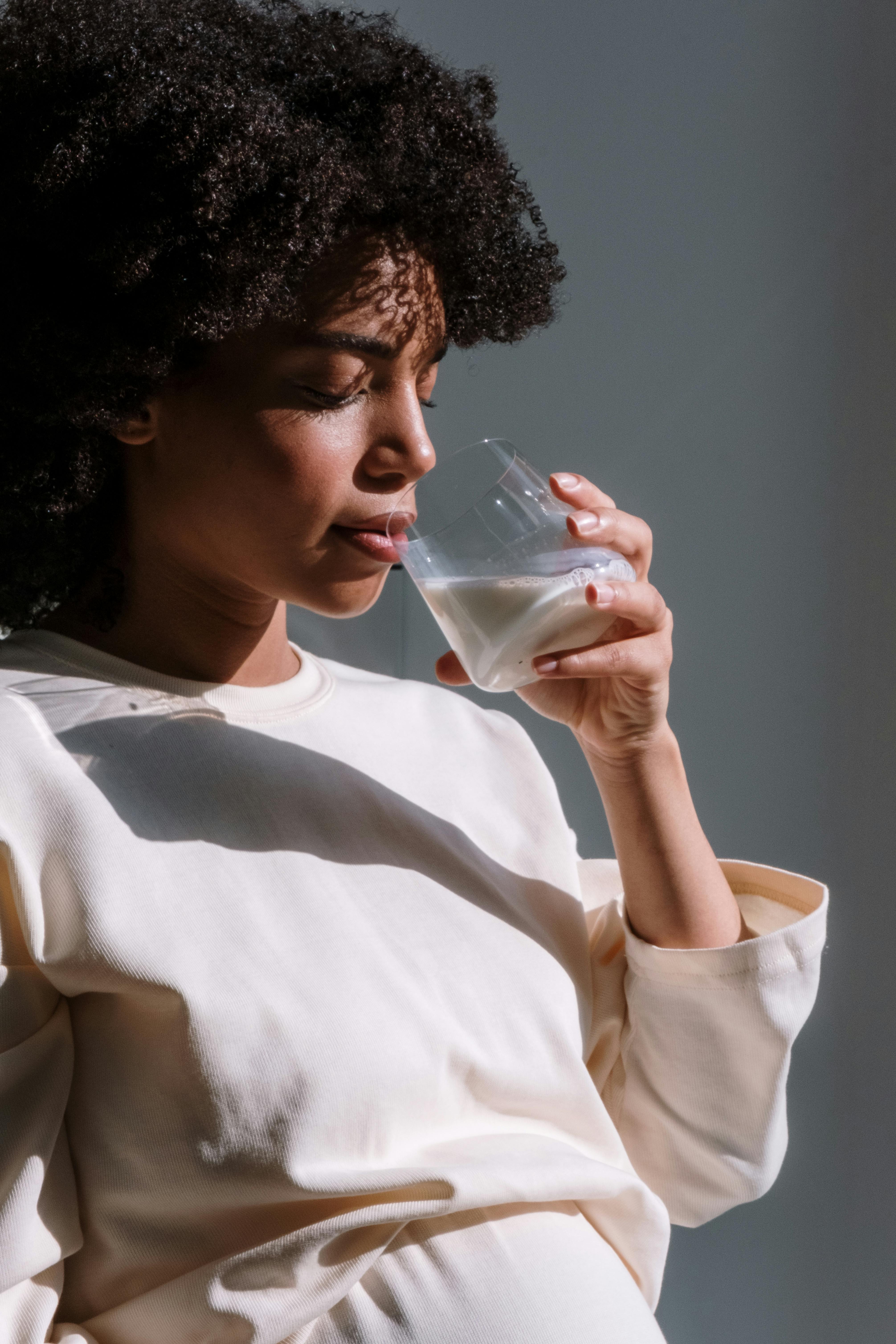 Person in white shirt drinking from a glass of milk.