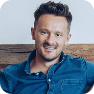A headshot of a smiling man with short brown hair wearing a blue button-up shirt.
