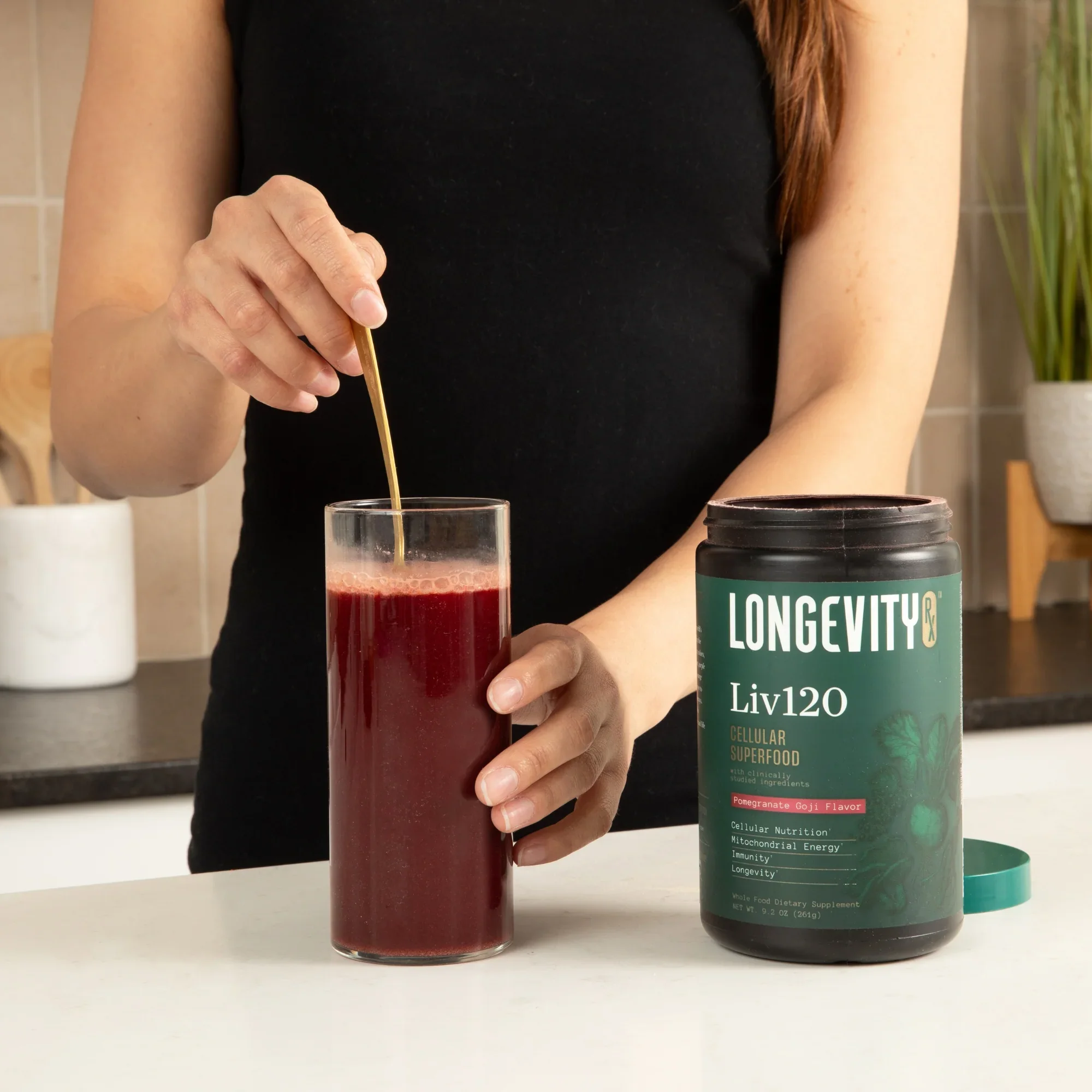 Person stirring red drink with spoon next to Longevity Liv120 container.